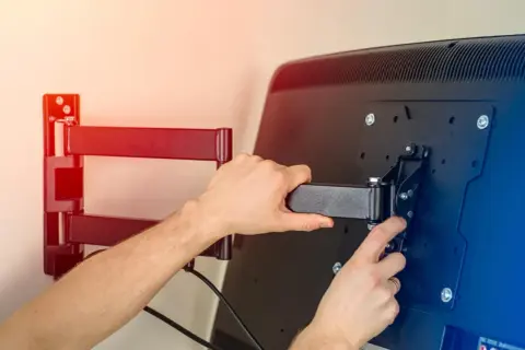 Ręce montują uchwyt do telewizora na ścianie. Dowiedz się, jak powiesić telewizor na ścianie, by cieszyć się kinem domowym.