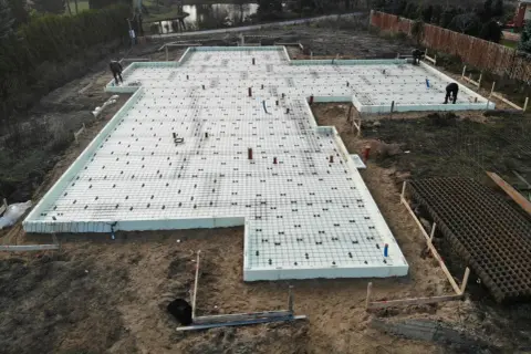 Prace nad fundamentem pod dom szkieletowy. Betonowanie płyty fundamentowej zbrojonej siatką i rurami.