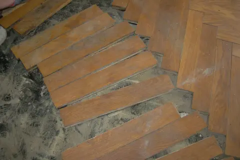 Drewniana podłoga w jodełkę, częściowo rozebrana. Widać pojedyncze deseczki i fragmenty ułożonego parkietu. Czy to subit?